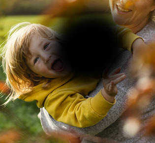 An image of a woman lifting a smiling child. The image has a black blob in the centre with blurred edges, obscuring the centre of the image.