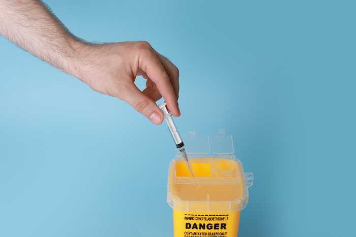 A hand putting a syringe into a yellow box